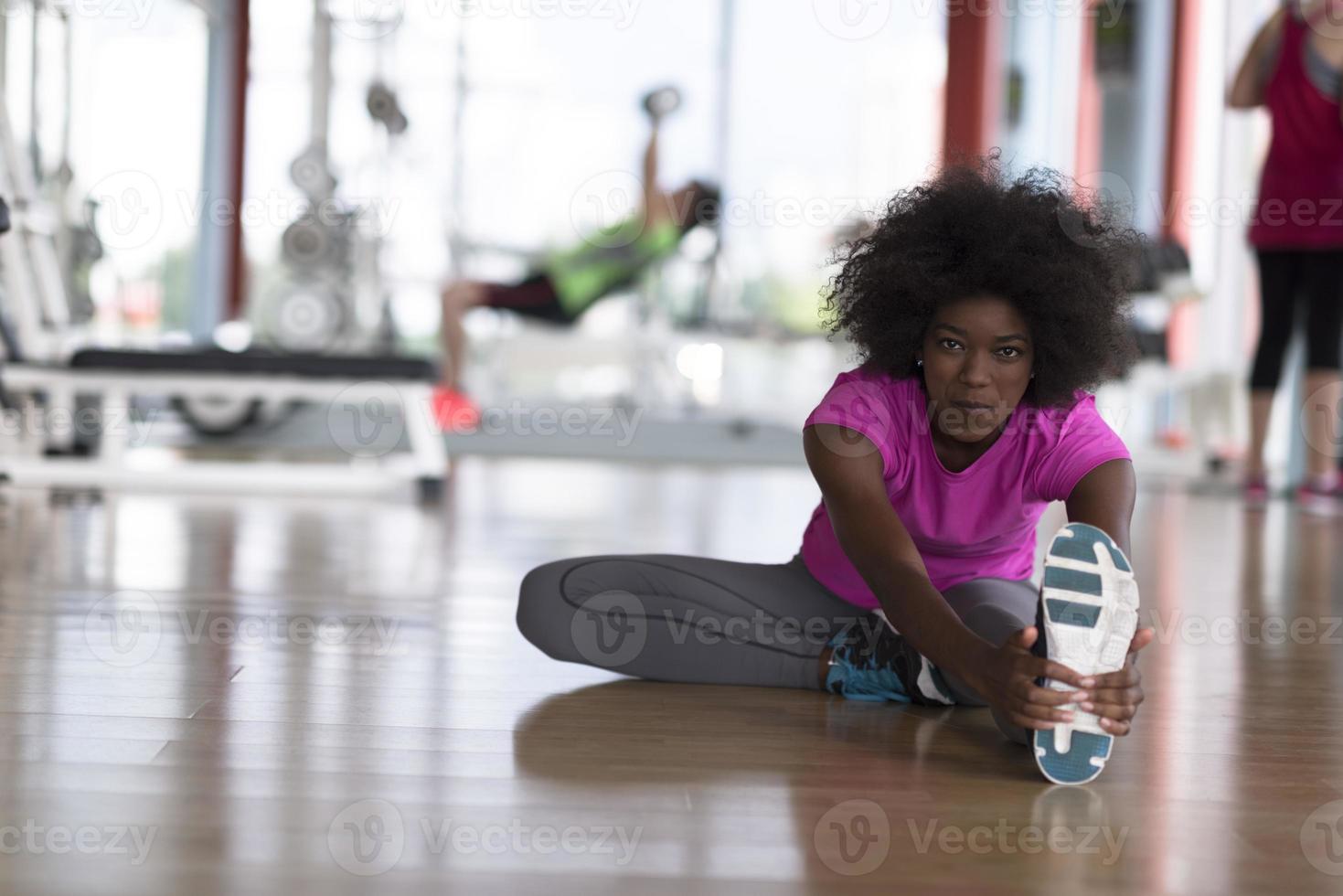 woman in a gym stretching and warming up man in background working with dumbbels photo