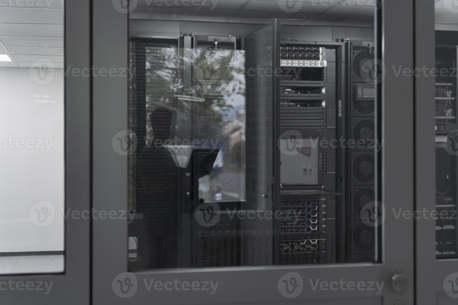 Software Engineer Working on a Laptop Computer in a Modern Server room. Monitoring Room Big Data Scientist in reflection of the entrance door. photo