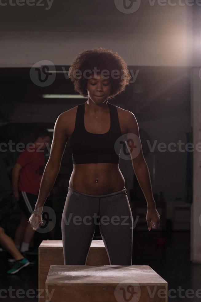 black female athlete is performing box jumps at gym photo