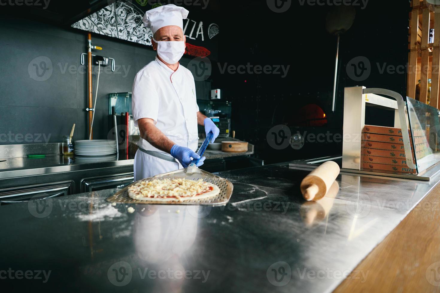 chef  with protective coronavirus face mask preparing pizza photo