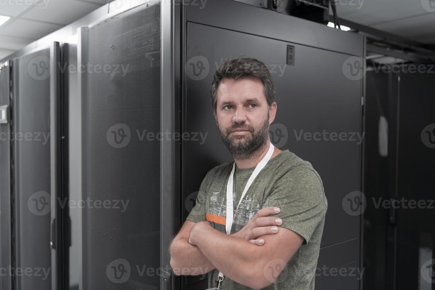 retrato de un técnico o administrador de red masculino que se muestra valiente como un héroe con los brazos cruzados en la sala de servidores del centro de datos. foto