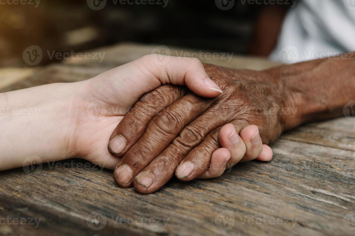 Hands of the old man and a woman hand on the wood table photo