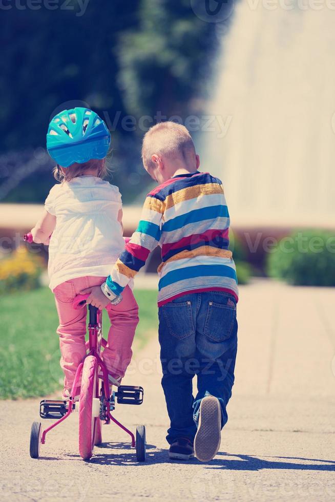 Boy and girl in park learning to ride a bike photo