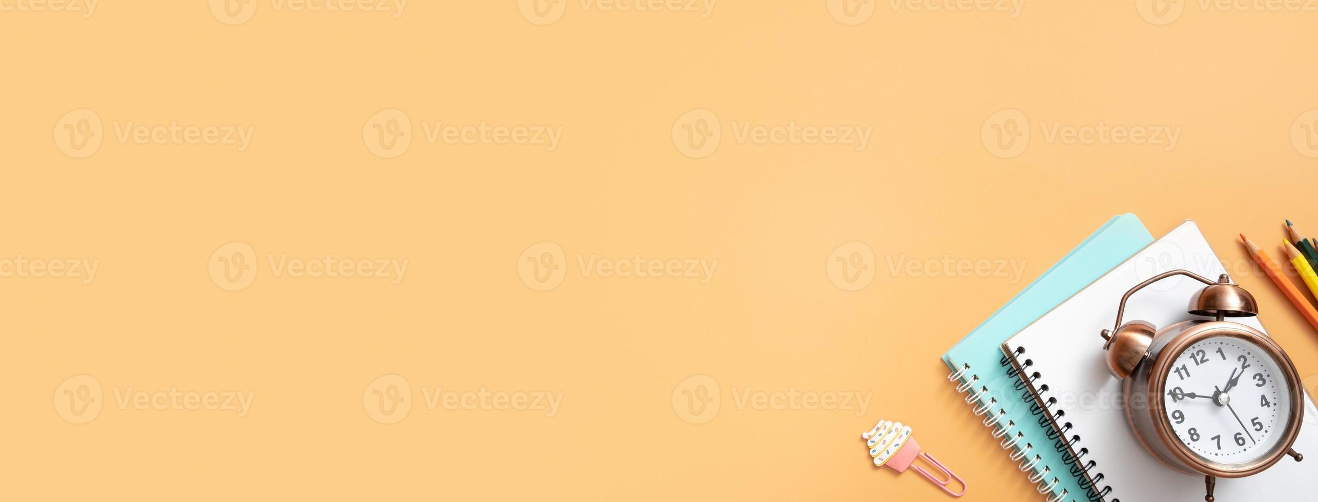 Notebooks, alarm clock and stationary on colored background. Copy space. Kids work space top view, flat lay. Online learning concept photo