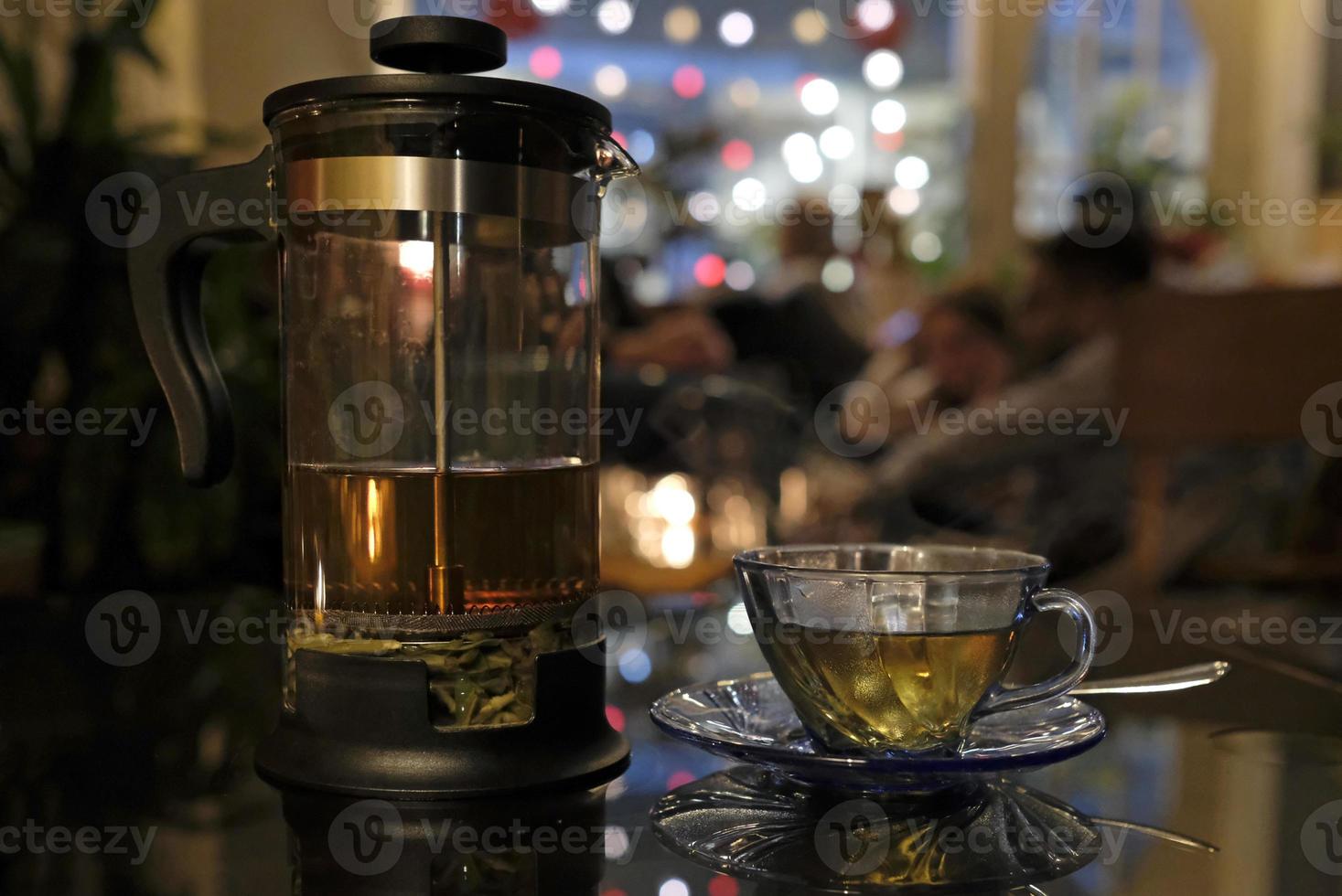 Fresh herbal tea in a transparent tea press in a cozy cafe in the evening photo