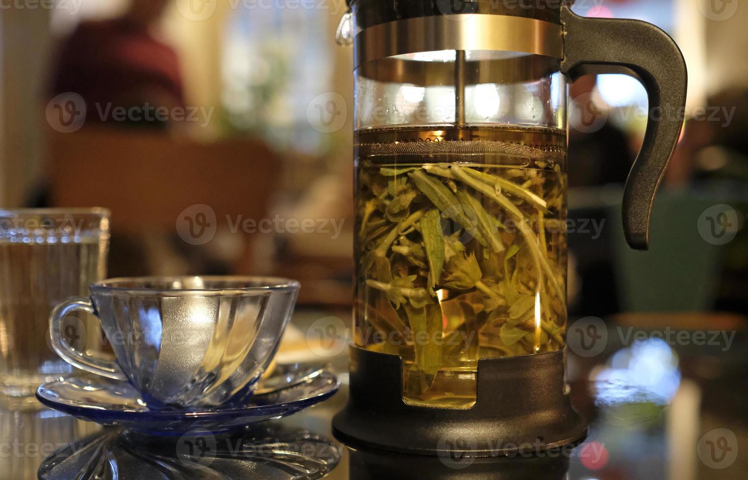 Fresh herbal tea in a transparent tea press in a cozy cafe in the evening photo