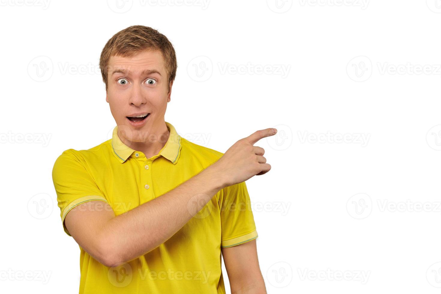 Surprised guy with funny face in bright yellow T-shirt pointing finger to right, white background photo