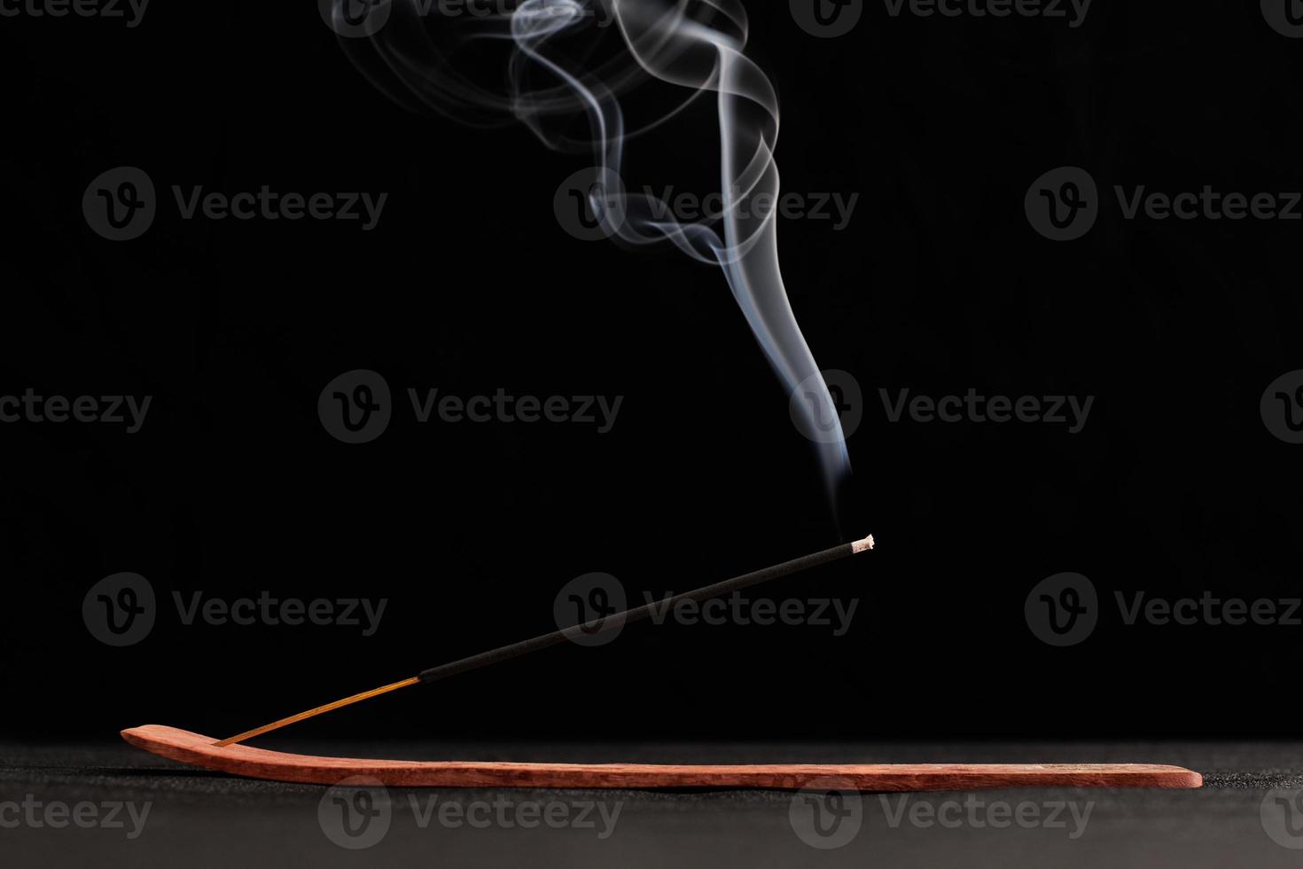 Smoke curls of burning incense stick in wooden holder for relaxation and meditation black background photo