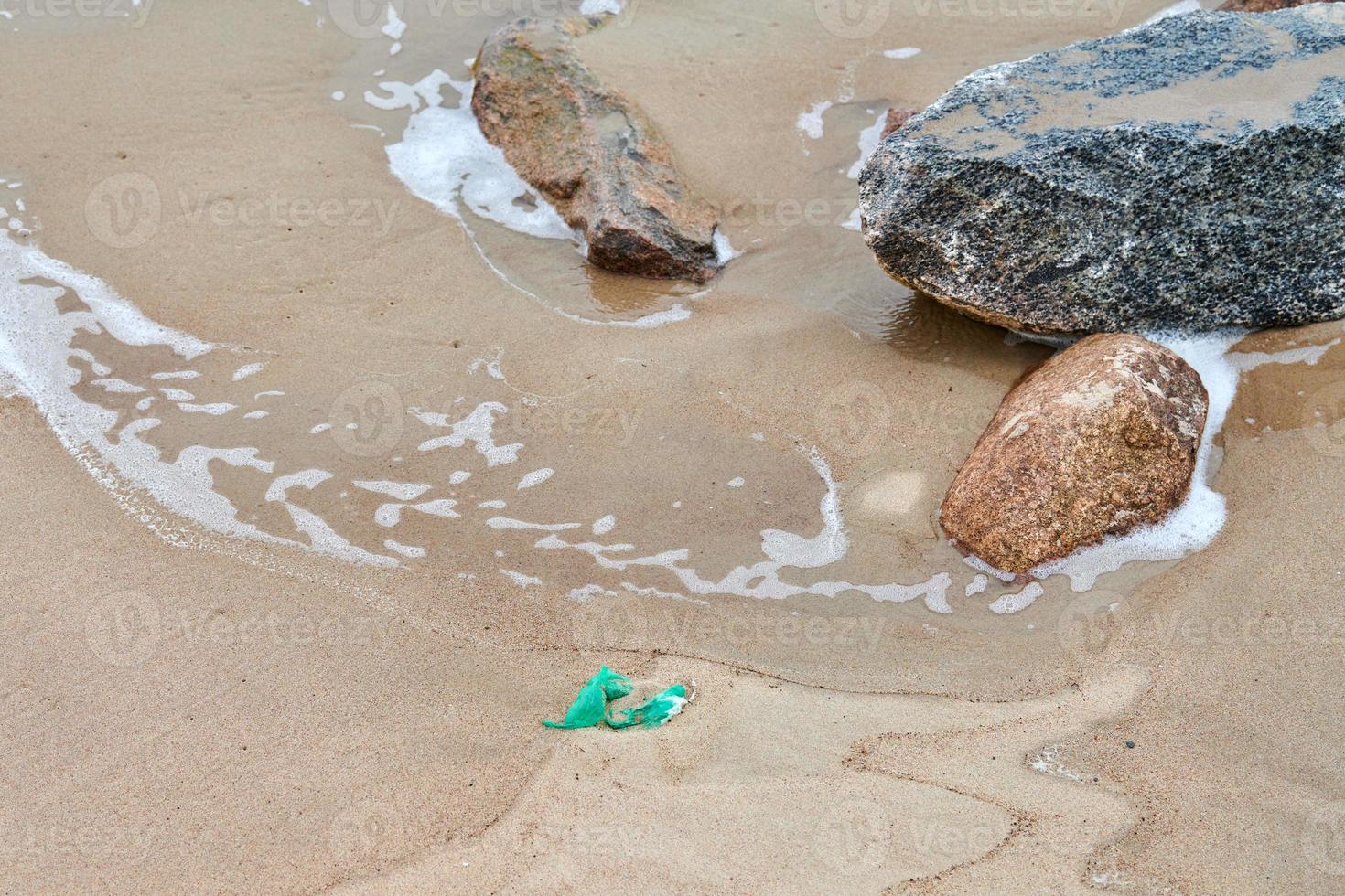 Empty used plastic green bag on sea sandy shore photo