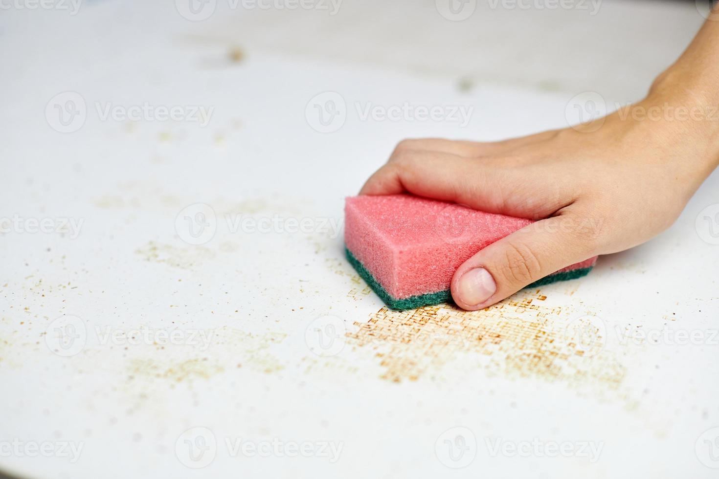 Sponge in woman hand removes dirt, bread crumbs and leftovers. Cleaning kitchen table. Household chores photo
