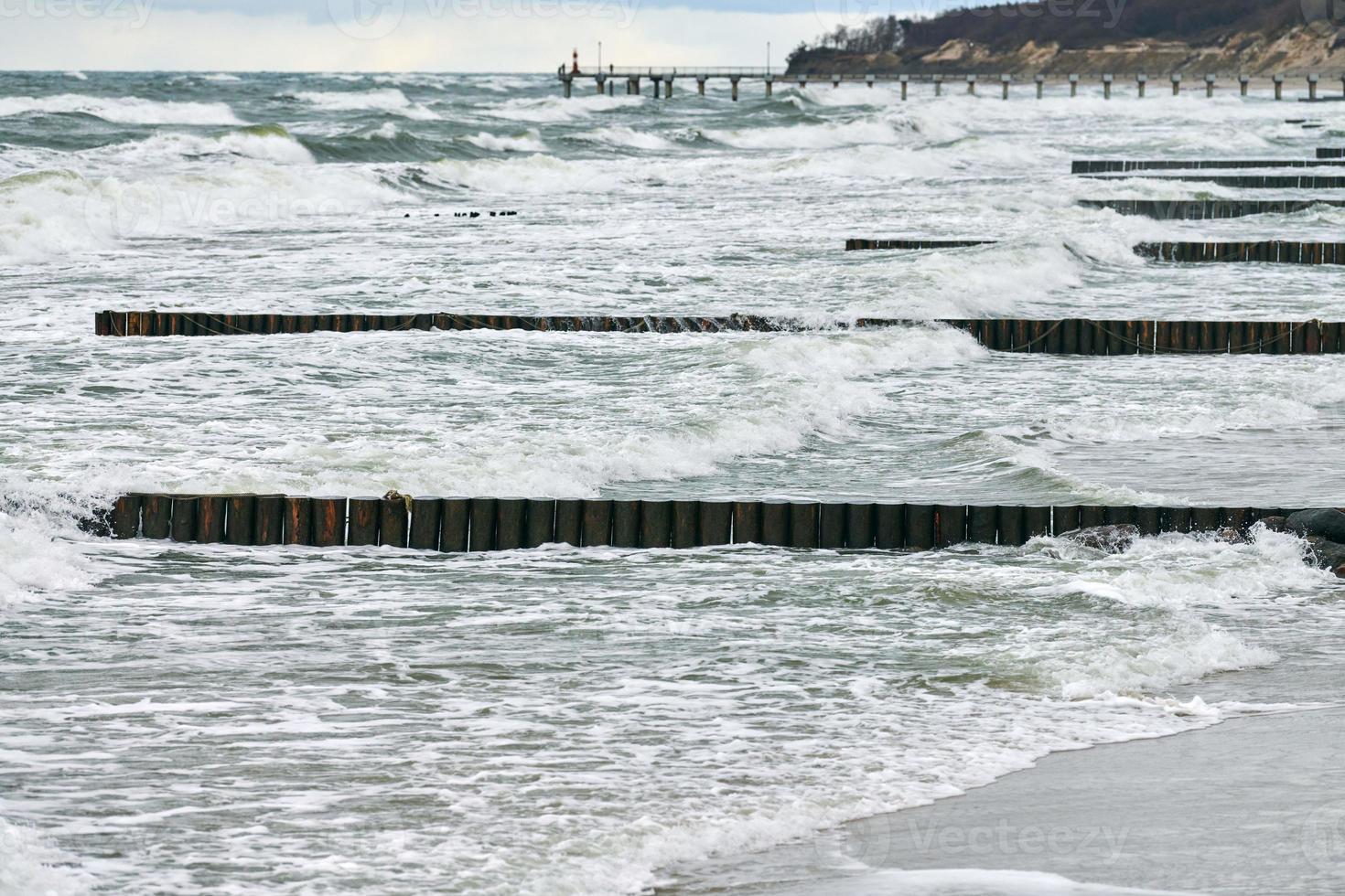 View of blue sea with foaming waves and wooden breakwaters photo