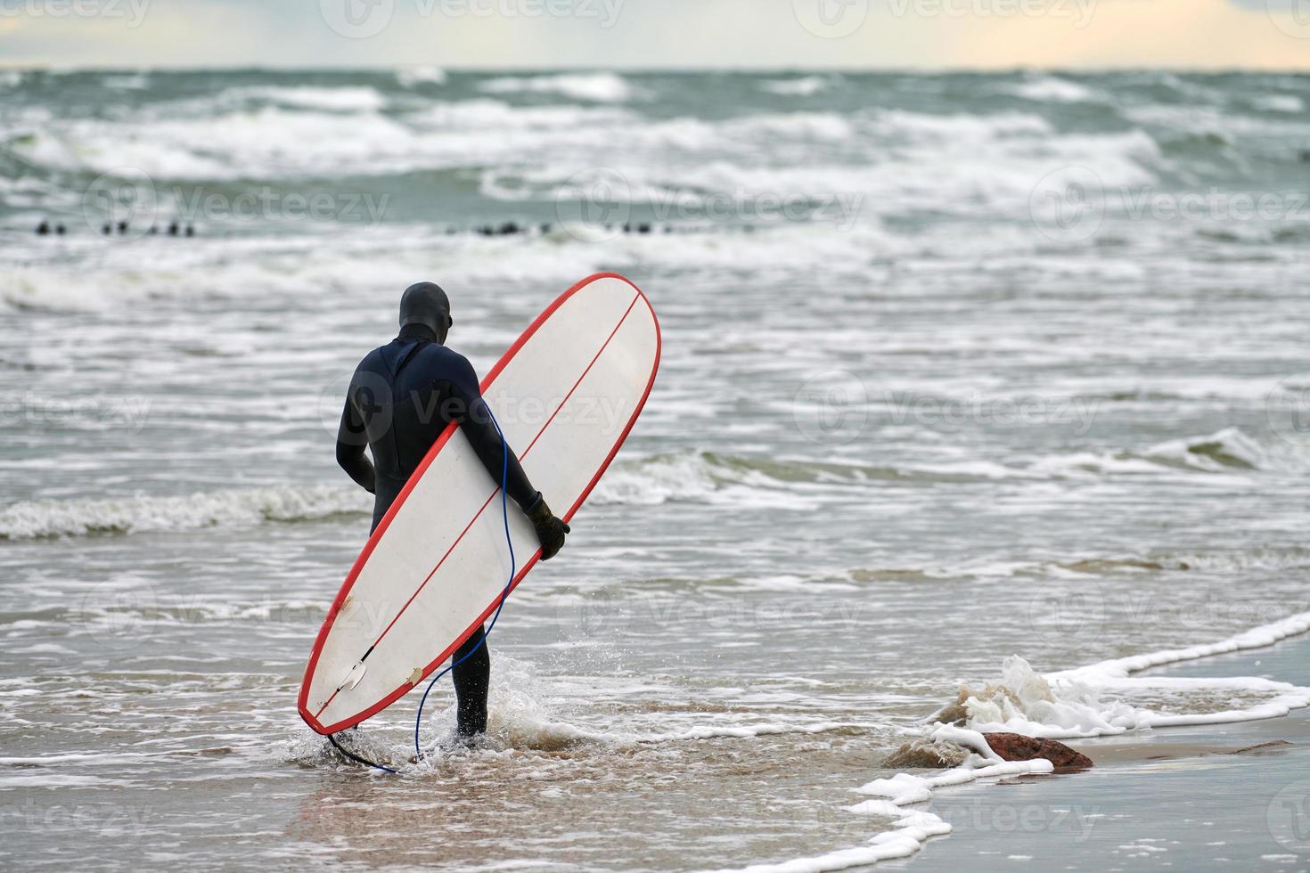 Male surfer in swim suit walking along sea with surfboard photo