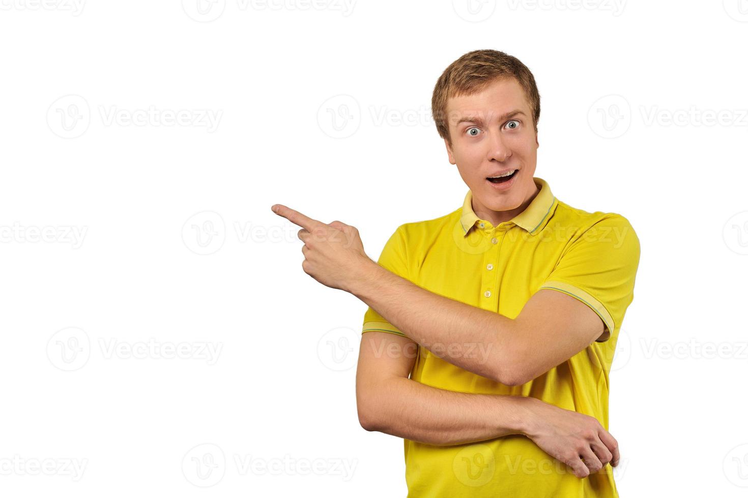 Surprised guy with funny face in yellow T-shirt pointing finger to left, white background photo