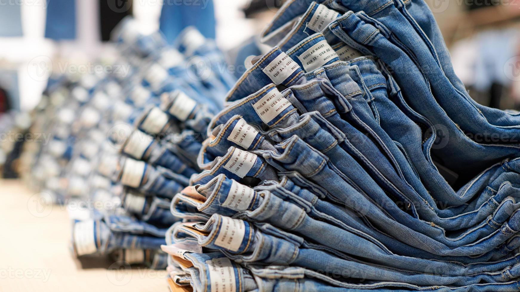 Denim jeans stack on wood table in clothing store, shopping photo