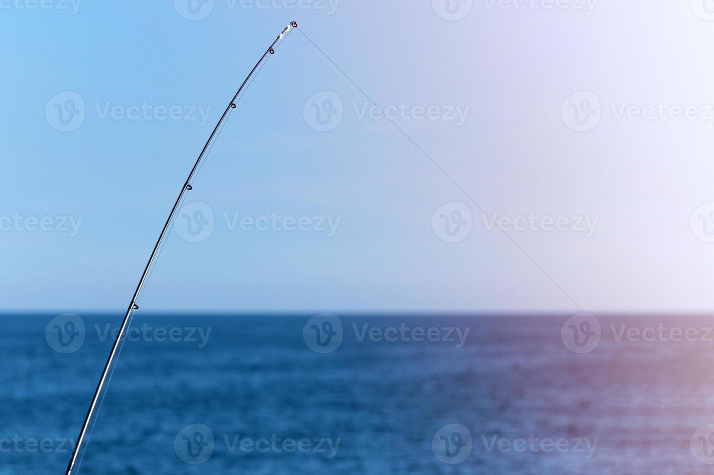 Fishing rod against blue ocean or sea background, copy space. Waiting for biggest haul. Meditative relax sport. photo