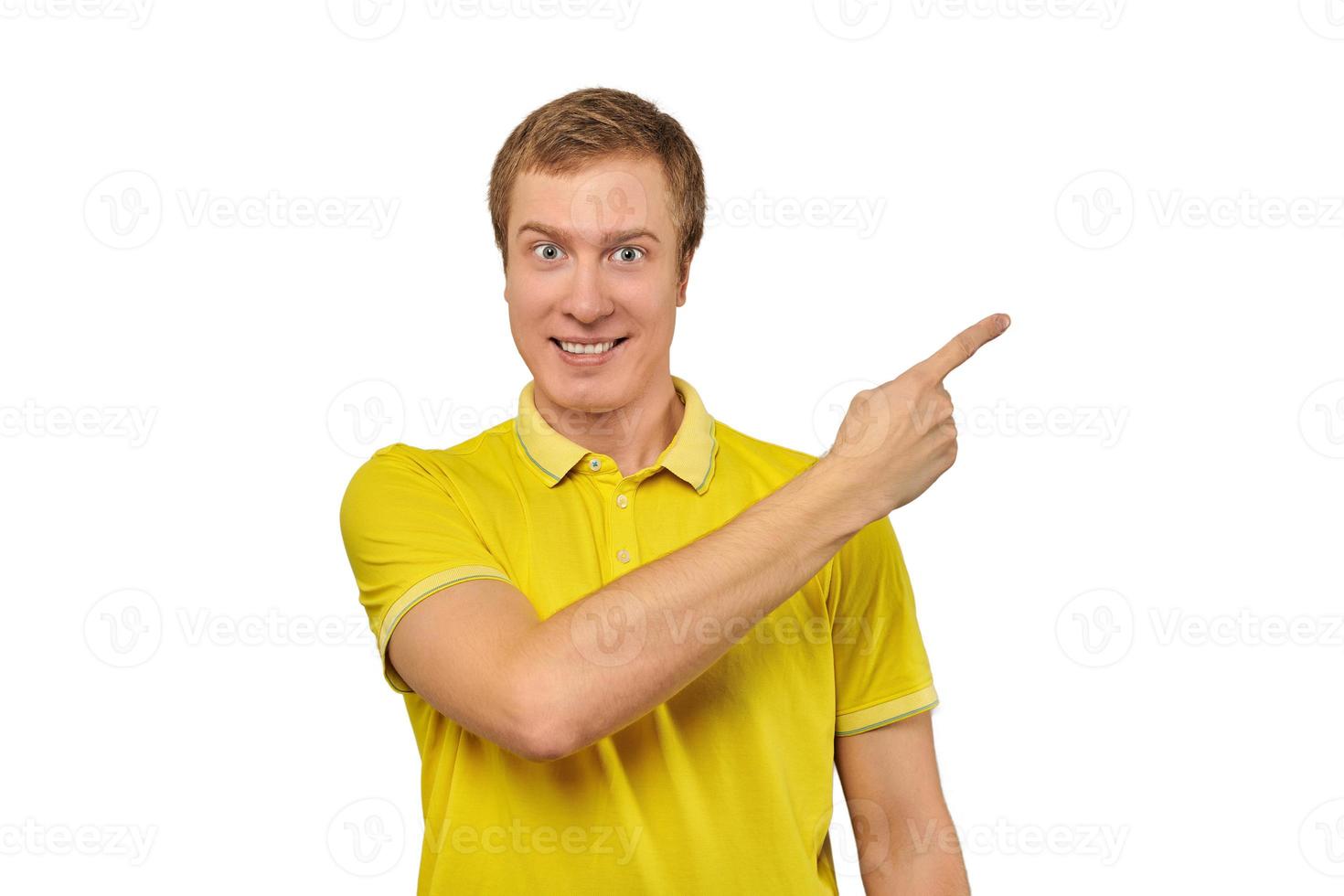 Smiling guy with funny face in yellow T-shirt pointing finger to right, white background photo