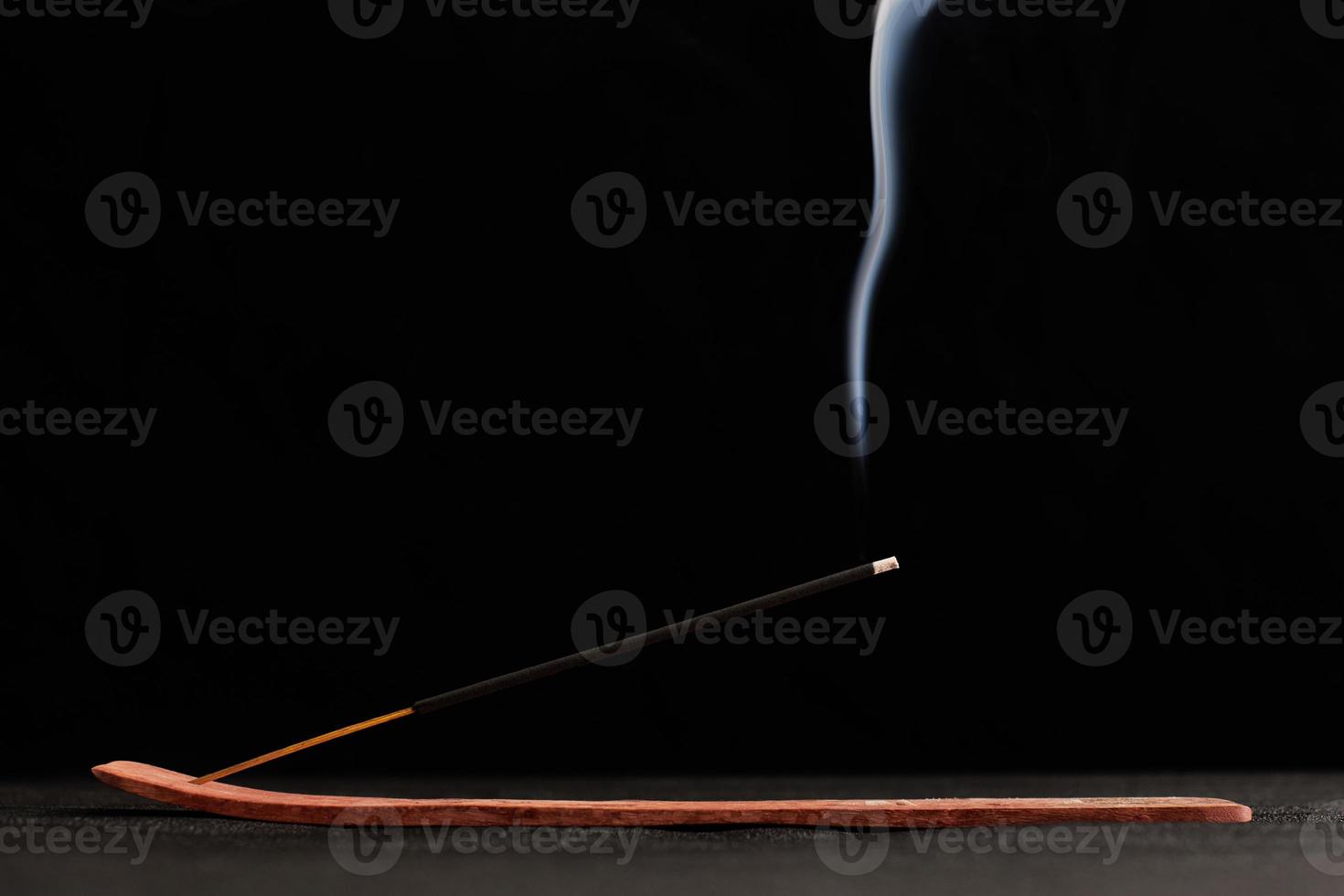 Smoke curls of burning incense stick in wooden holder for relaxation and meditation black background photo