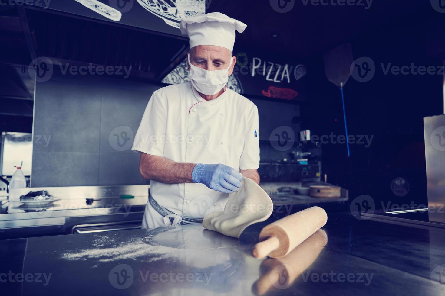 chef  with protective coronavirus face mask preparing pizza photo