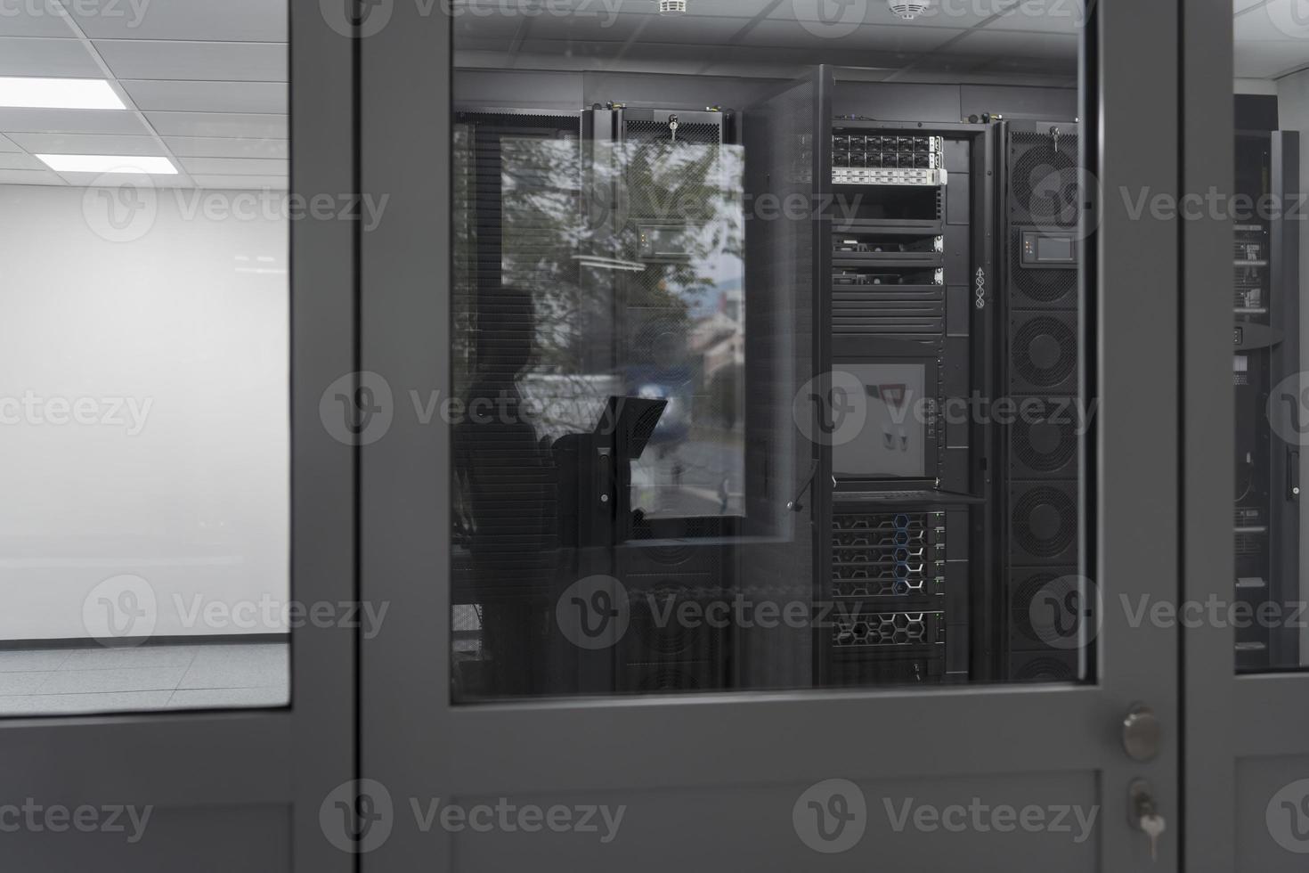 Software Engineer Working on a Laptop Computer in a Modern Server room. Monitoring Room Big Data Scientist in reflection of the entrance door. photo