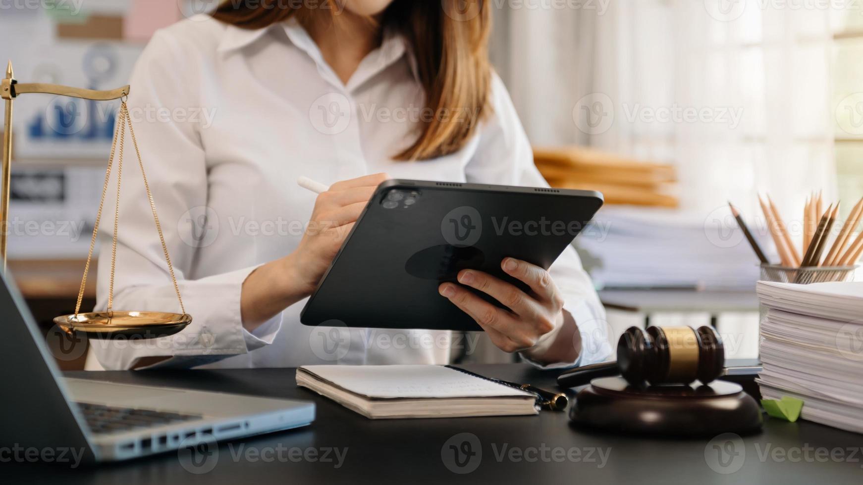 concepto de justicia y derecho. juez masculino en una sala de audiencias con el mazo, trabajando con tableta, computadora y teclado de acoplamiento, anteojos, en la mesa foto