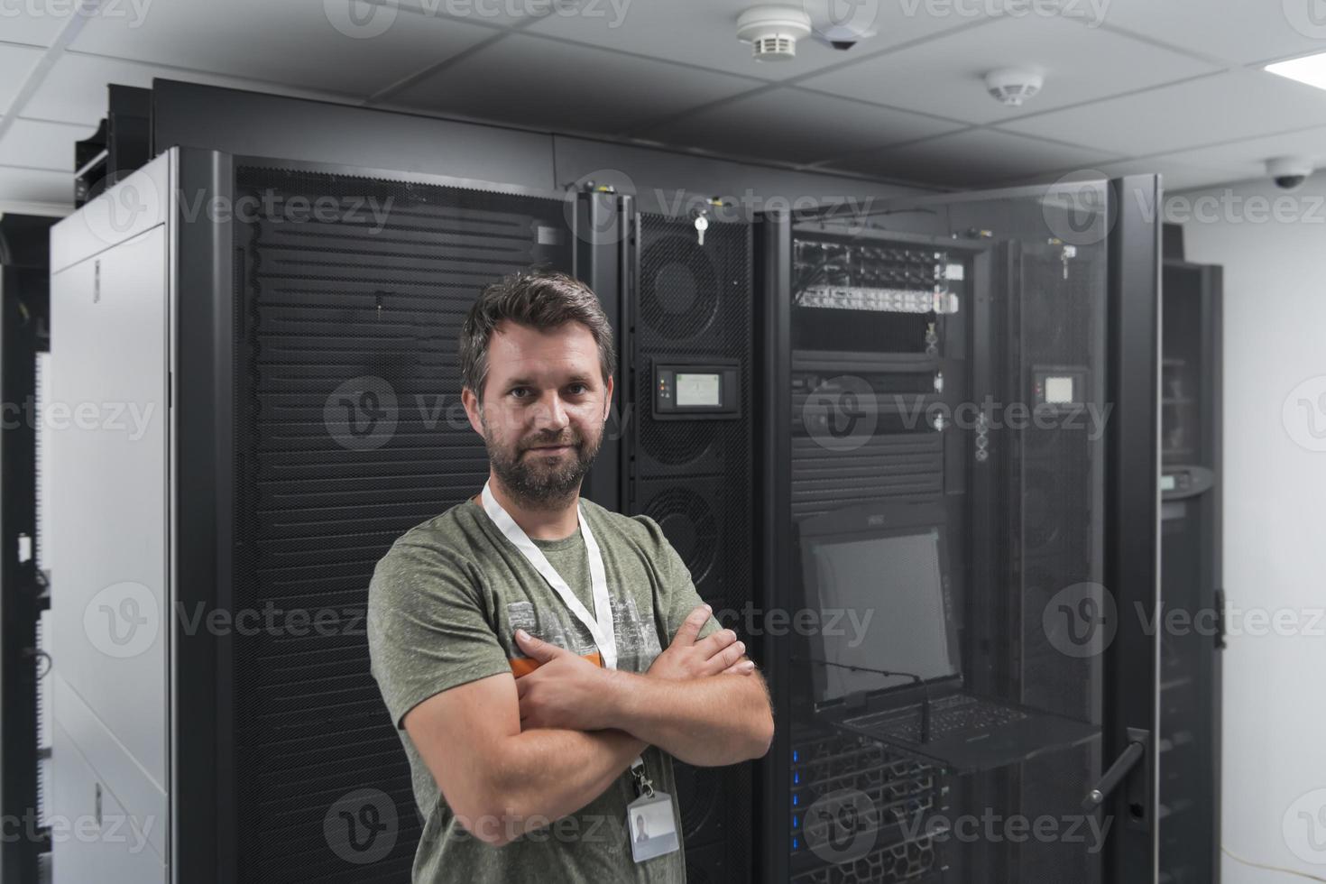 retrato de un técnico o administrador de red masculino que se muestra valiente como un héroe con los brazos cruzados en la sala de servidores del centro de datos. foto