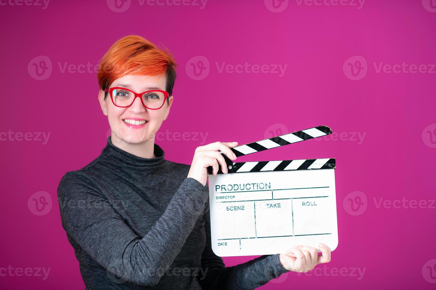 redhead woman holding movie  clapper on pink background photo