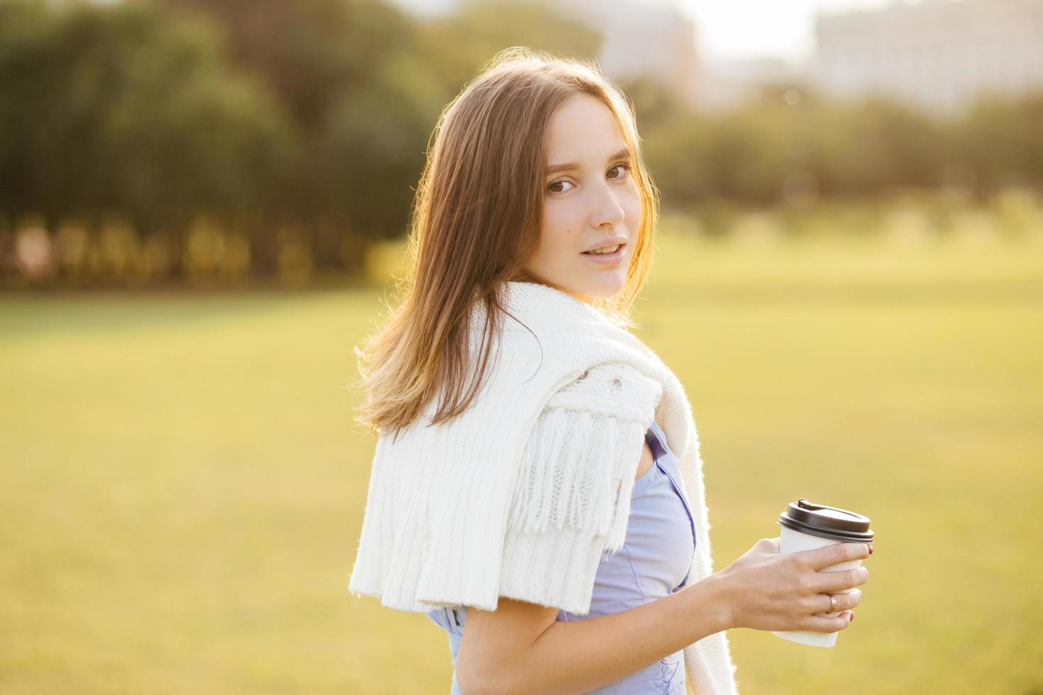 toma lateral de una linda joven con har oscuro, sostiene una taza con café o capuchino, respira aire fresco, disfruta de un ambiente tranquilo, admira la hermosa naturaleza y la puesta de sol. concepto de personas y estilo de vida foto