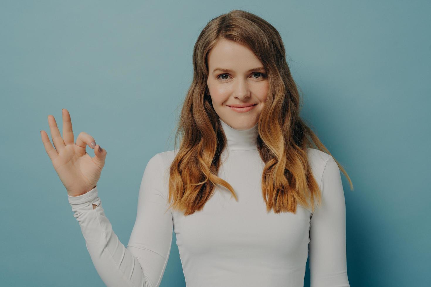 Cheerful young european woman showing okay gesture isolated over pastel blue studio wall photo