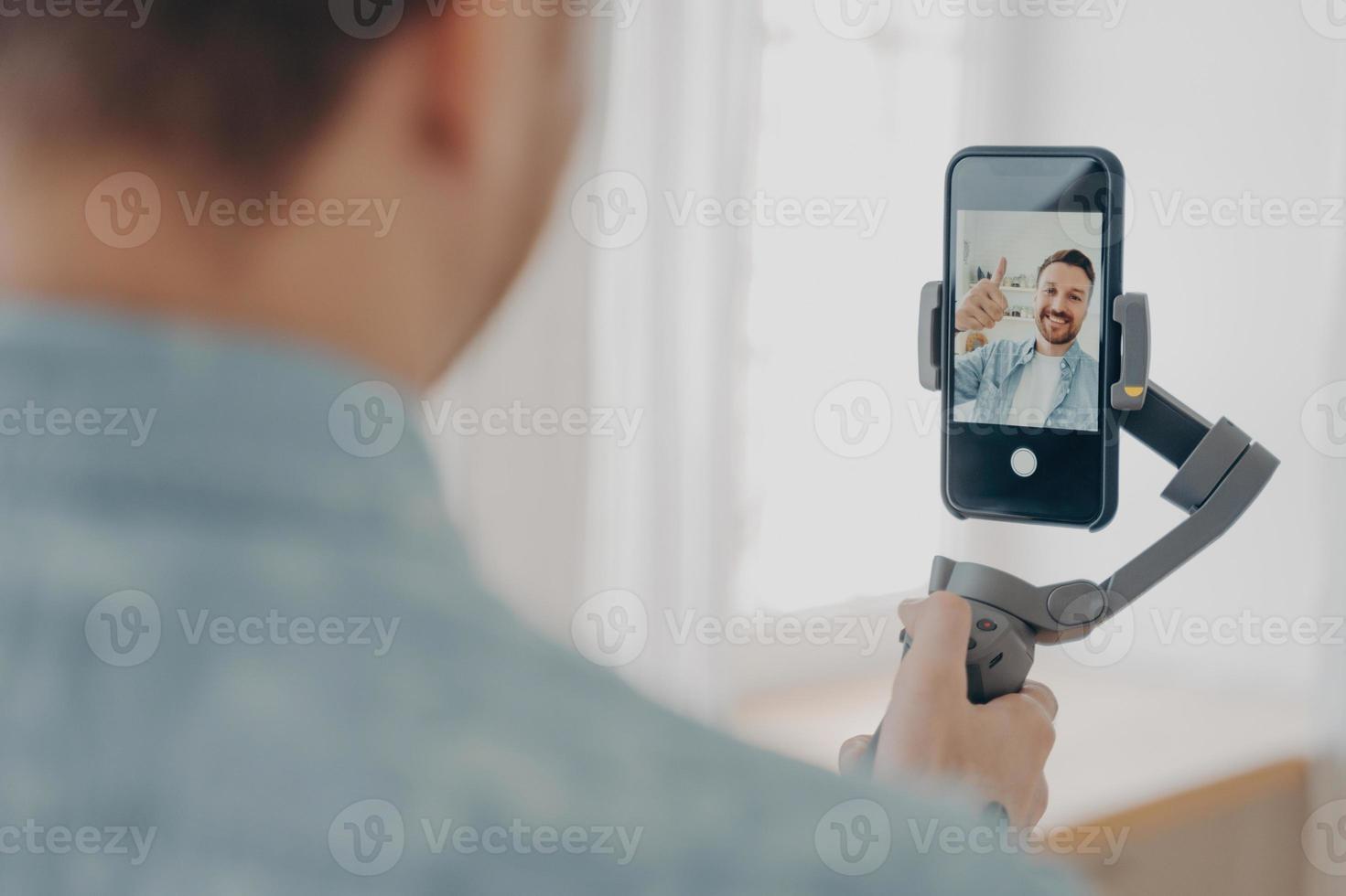 apuesto joven brunete sonriente con rastrojo haciendo selfie en smartphone foto