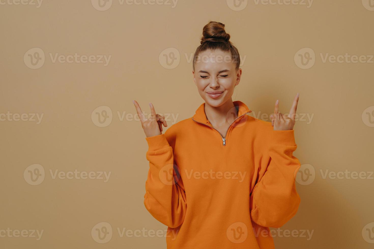 Overjoyed young woman showing rock-n-roll gesture, celebrating achievement with closed eyes photo
