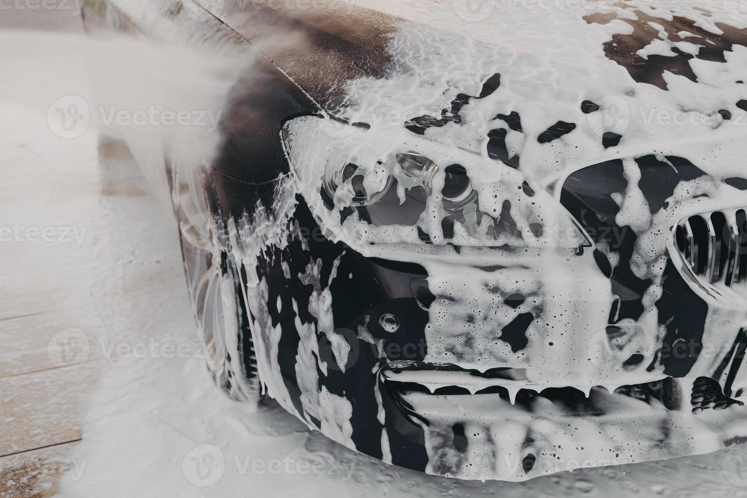 Black car in white snow foam during carwashing and cleaning outdoors photo