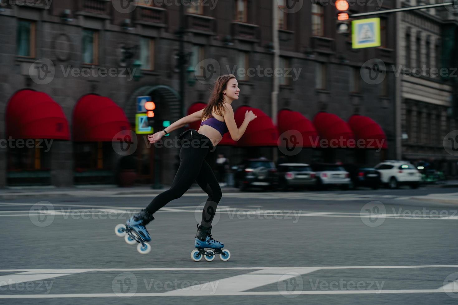 Extreme sport recreation and fitness activity concept. Active woman rides on rollers in urban environment strengthens leg muscles demonstrates high level of stability balances on small wheels photo