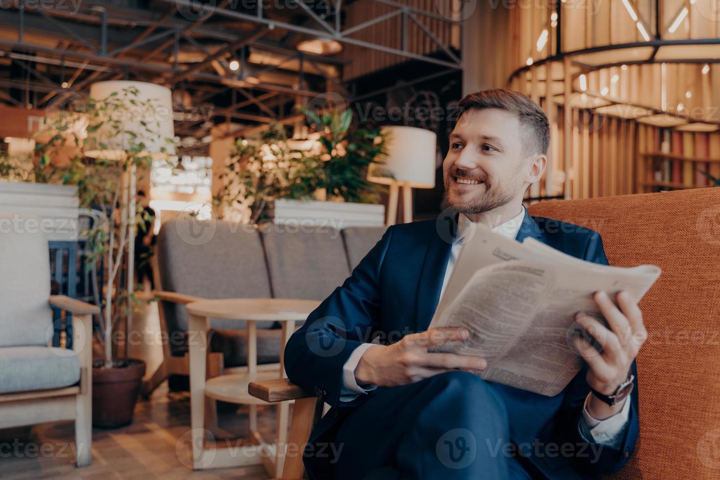 Positive young businessman reading newspaper in cafe photo