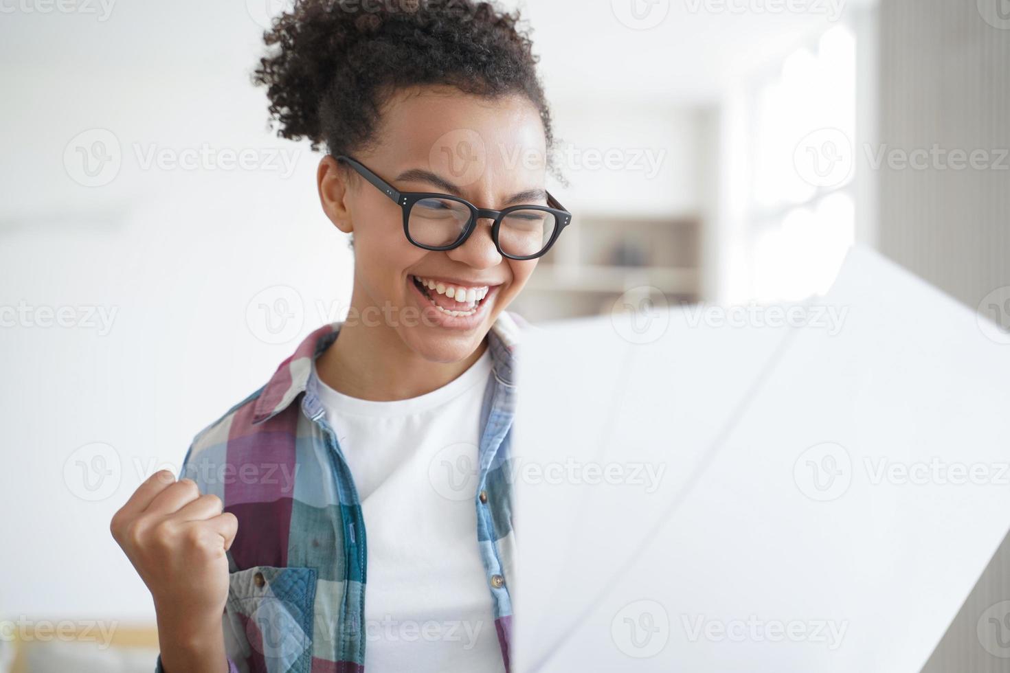Excited spanish schoolgirl is winner holding letter. Afro teenage girl pupil is accepted to college. photo