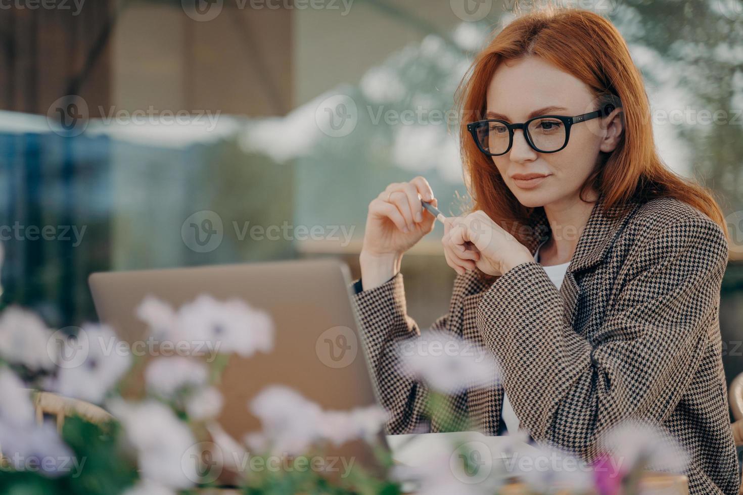 joven mujer de negocios pelirroja enfocada trabaja en línea en un café al aire libre foto
