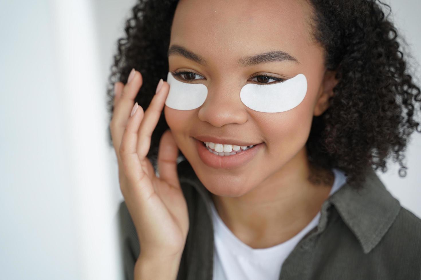 Young biracial girl applying under eye patches for healthy fresh face skin. Skincare, beauty routine photo
