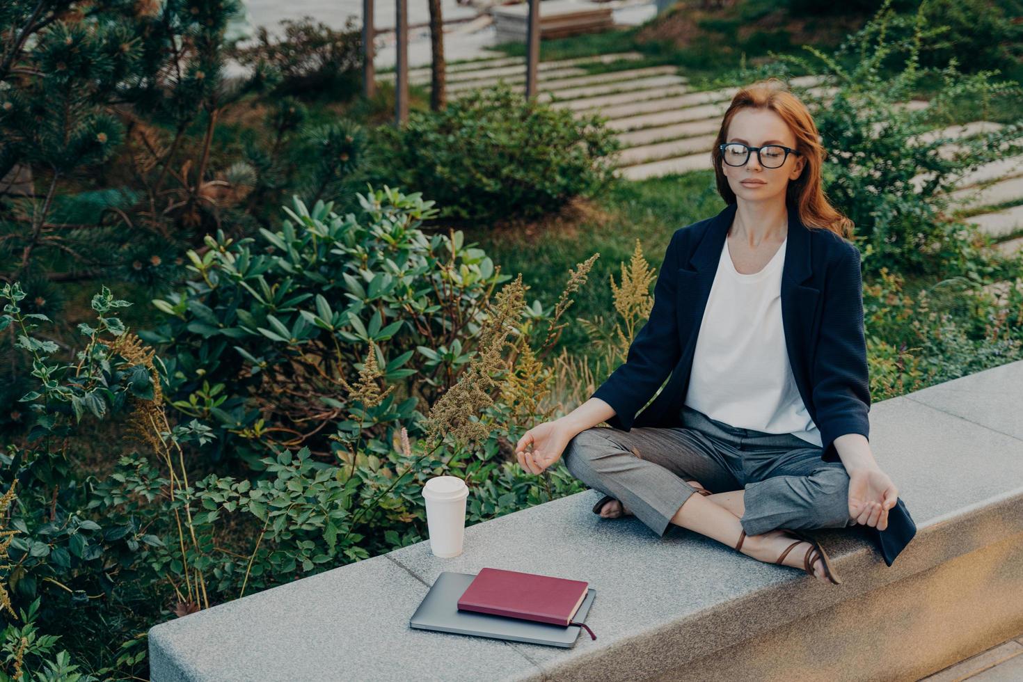 Peaceful calm redhead business woman doing yoga with closed eyes outdoor photo