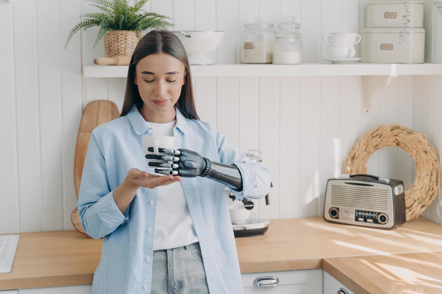 Pretty disabled girl is holding cup of tea with cyber hand carefully. Concept of grasp sensors. photo