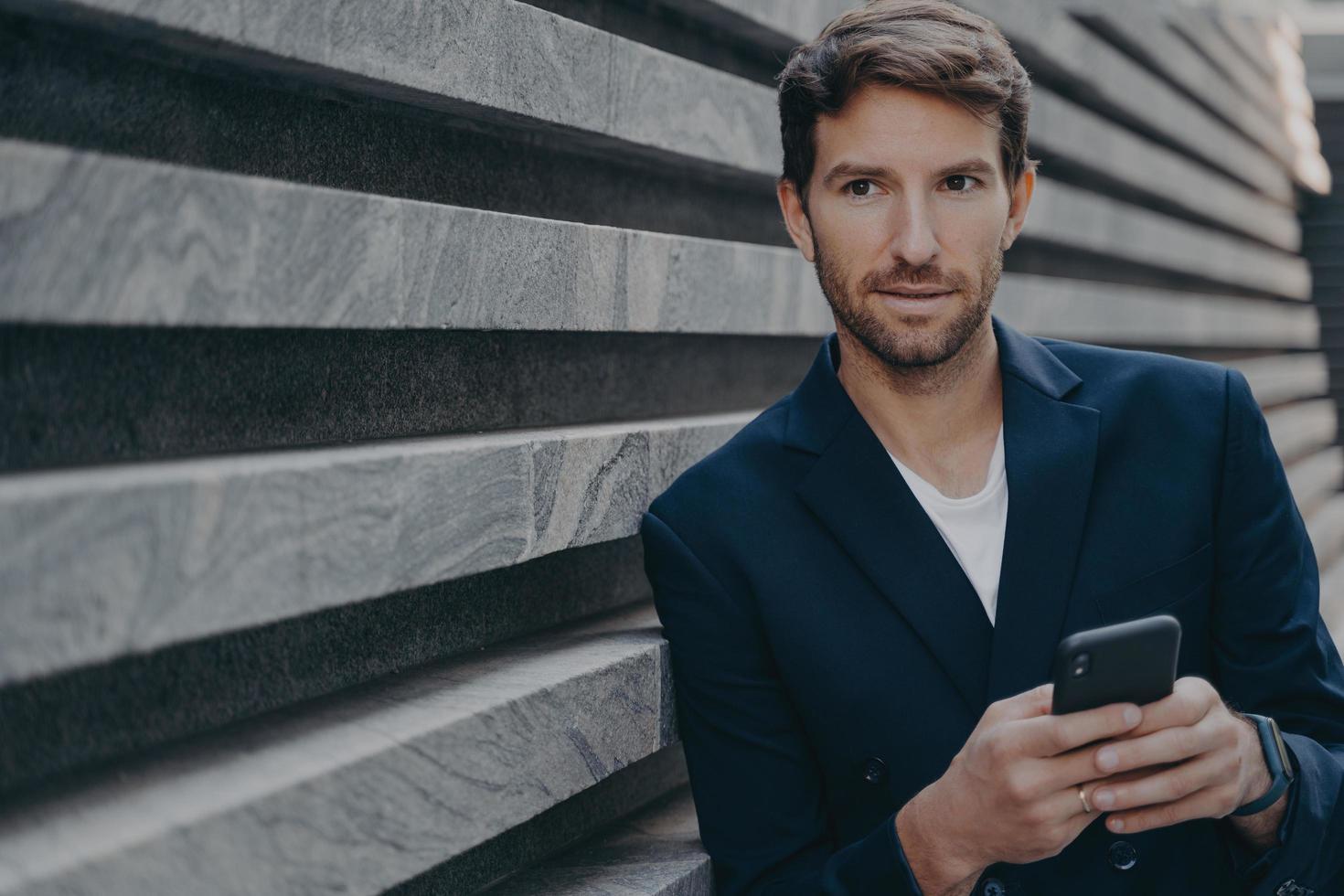 Businessman looks thoughtfully into distance uses smartphone thinks about future career success photo