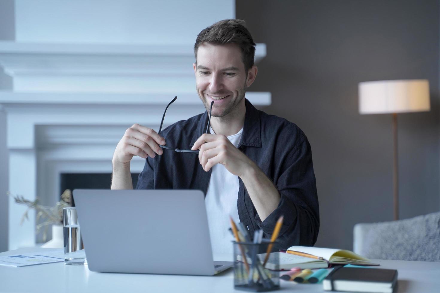 Exited german man freelancer looking on laptop with happy smile while holding glasses in hands photo