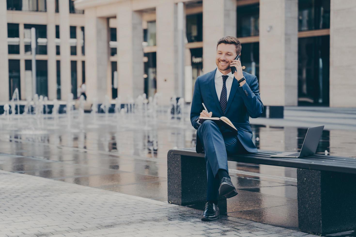 Successful businessman talking on mobile phone while working outside, sitting on bench photo