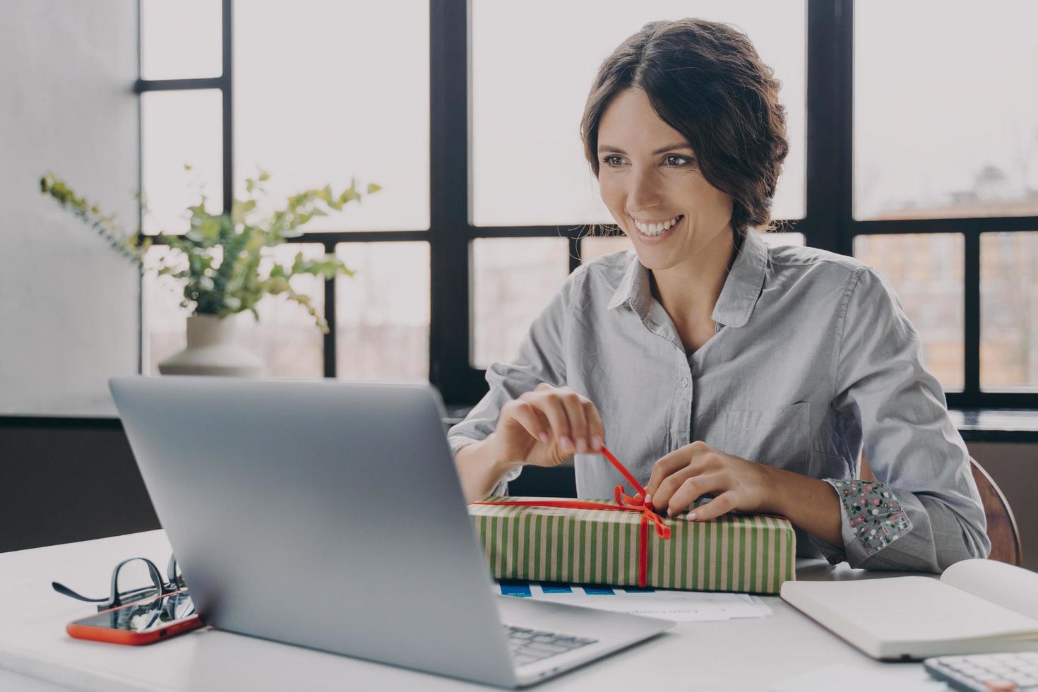 feliz alegre mujer italiana trabajadora de oficina en casa se sienta en el escritorio desempaca el regalo de año nuevo recién recibido foto