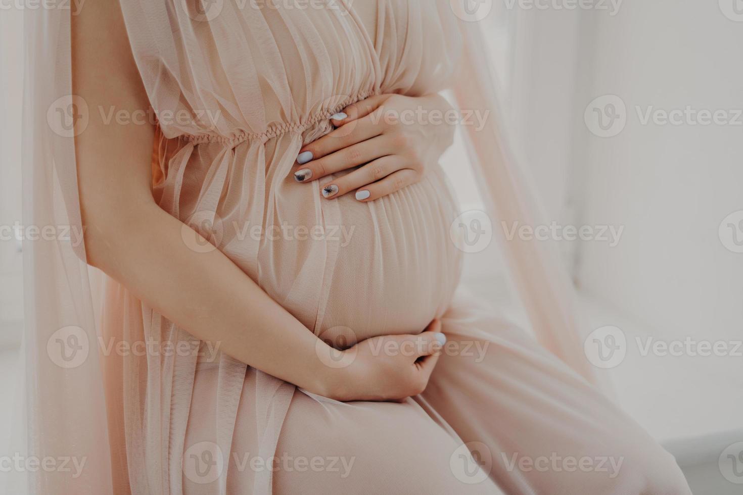 la imagen recortada de una mujer sin rostro toca su abdomen anticipa que el bebé usa poses de vestimenta festiva en el interior. concepto de mujer y embarazo foto