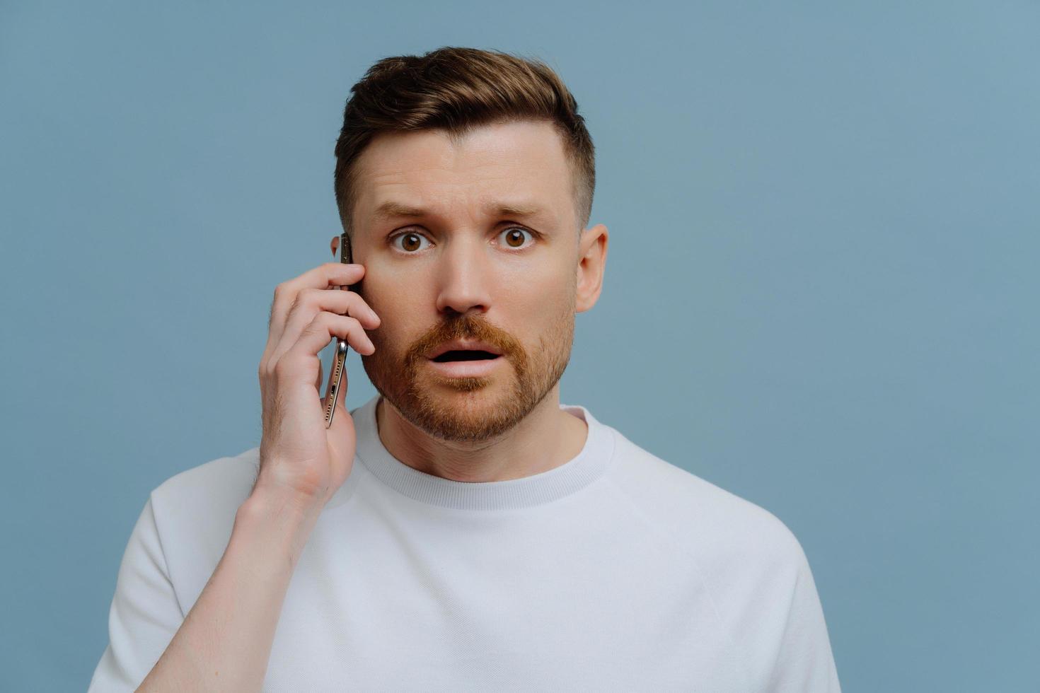 Surprised man receiving shocked news while talking with somebody on mobile phone photo