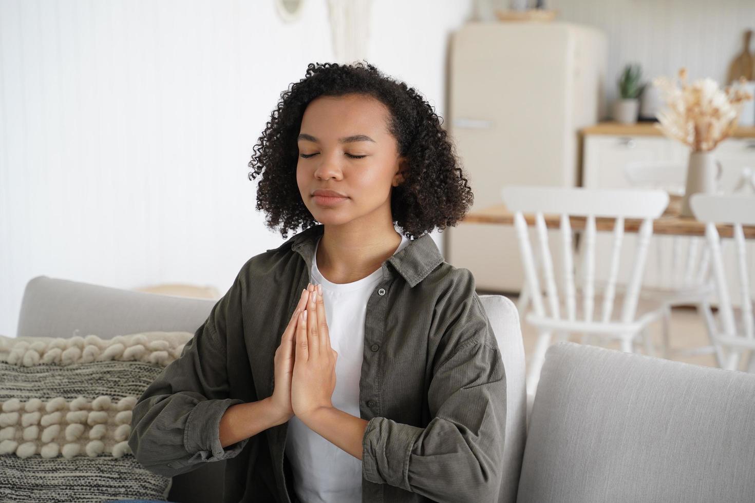 una adolescente afroamericana está practicando yoga en casa. la mujer está sentada en el sofá en posición de loto. foto