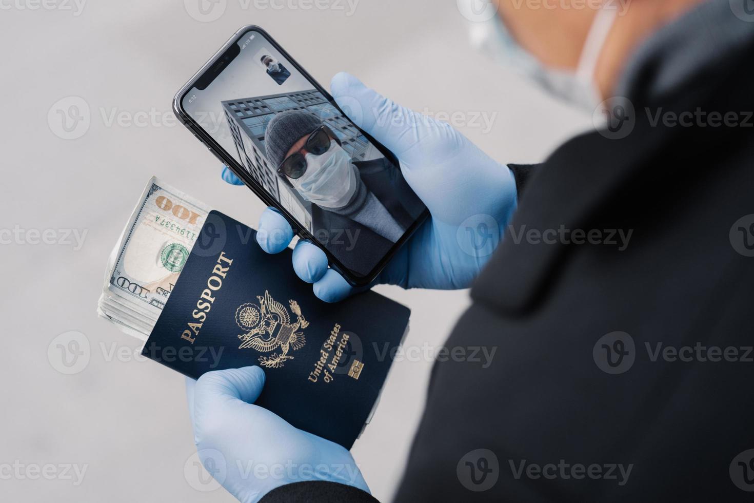 Online communication, quarantine and social distancing concept. Unknown man holds mobile phone, has video conference with friend, carries passport and much money, cares about health, wears mask photo