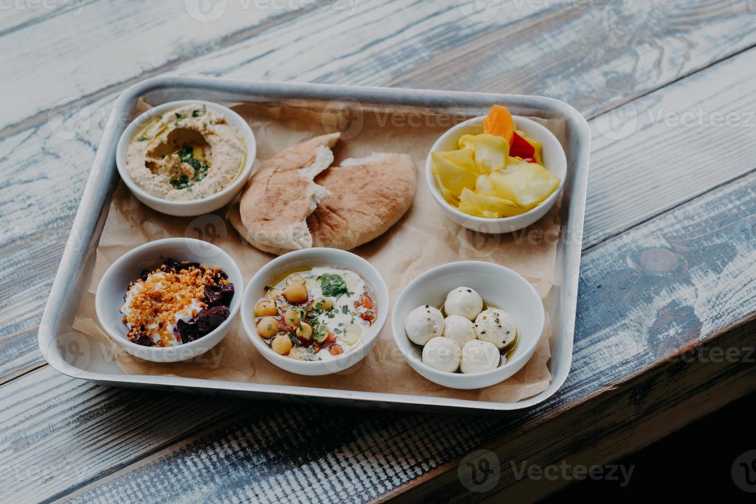 Traditional Israel food concept. Bowl of exotic dish on tray. Hummus, vegetables with spices. Pita bread. Delicious breakfast. Goat cheese. photo