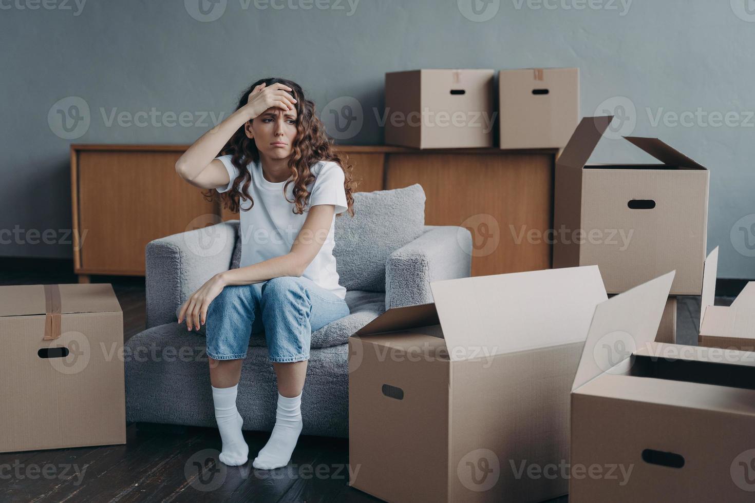 Headache from moving. Exhausted spanish woman sitting among packed cardboard boxes. photo