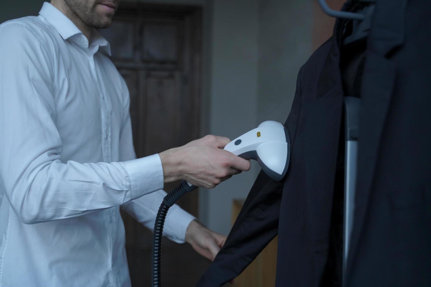 Businessman preparing clothes for meeting with partner, steaming suit with portable steamer photo