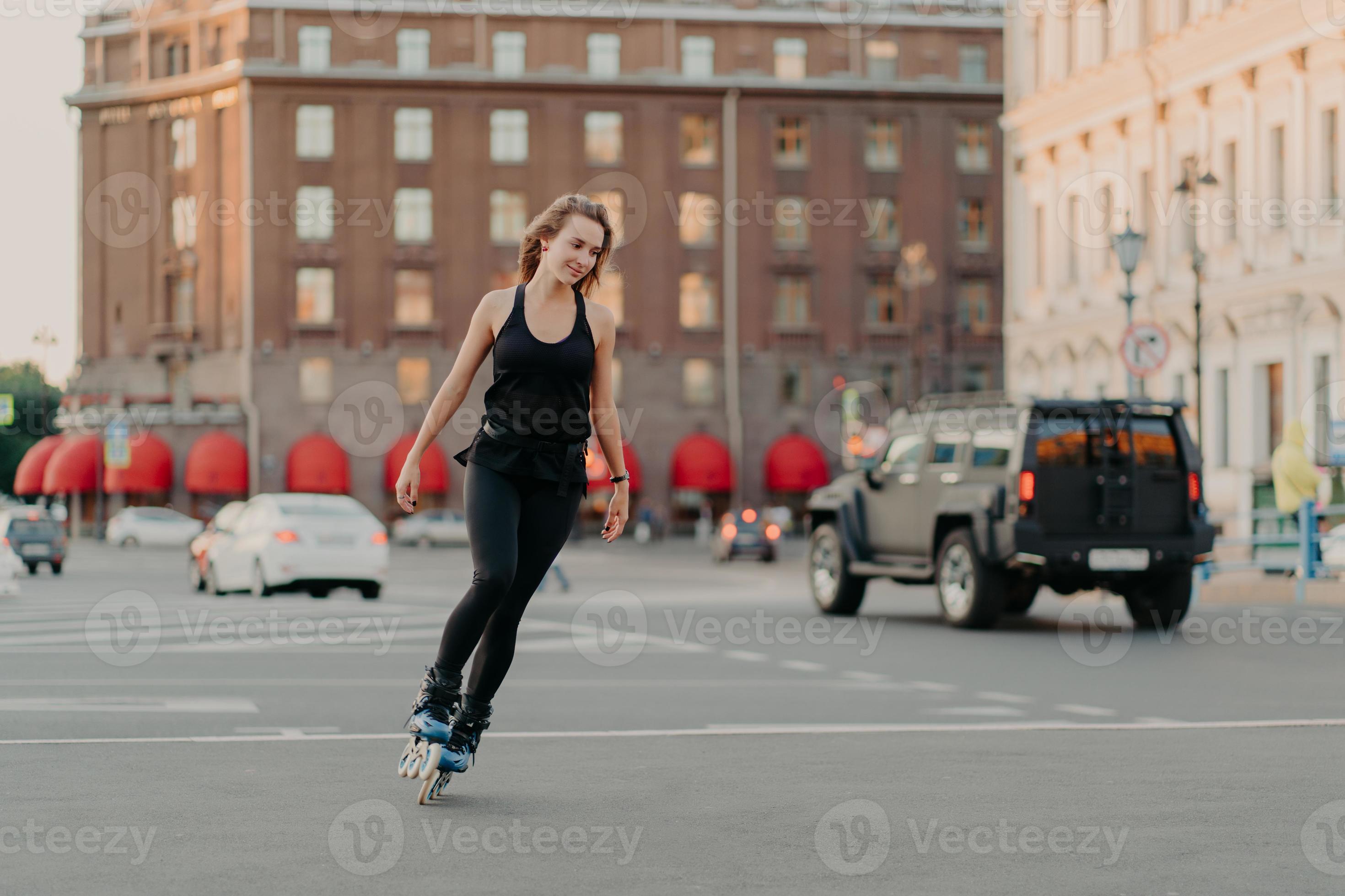 Active girl rollerblading on grey asphalt poses on rollers dressed in